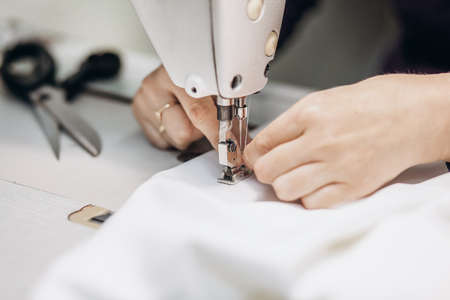 186397495-hands-of-a-dressmaker-sewing-clothes-from-white-fabric-on-a-sewing-machine-close-up